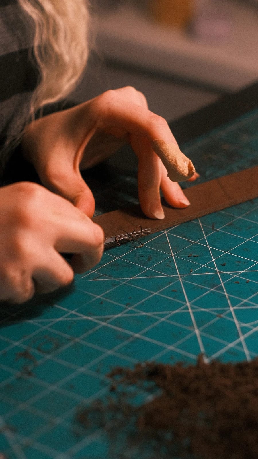 Hands working along the edge of a leather strap on a cutting mat