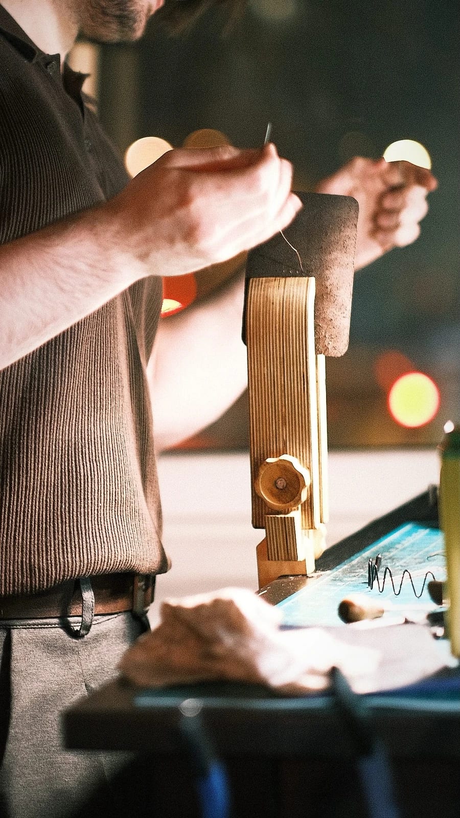 A hand stitching a leather strip held in a wooden clamp