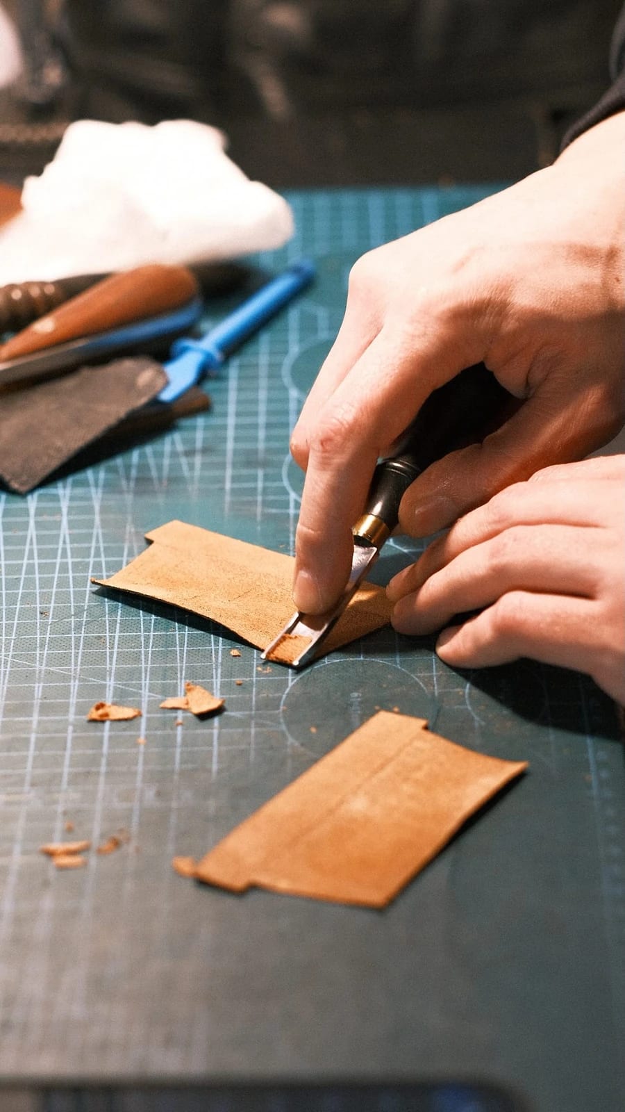 Hands paring the edge of a leather strip on the cutting mat