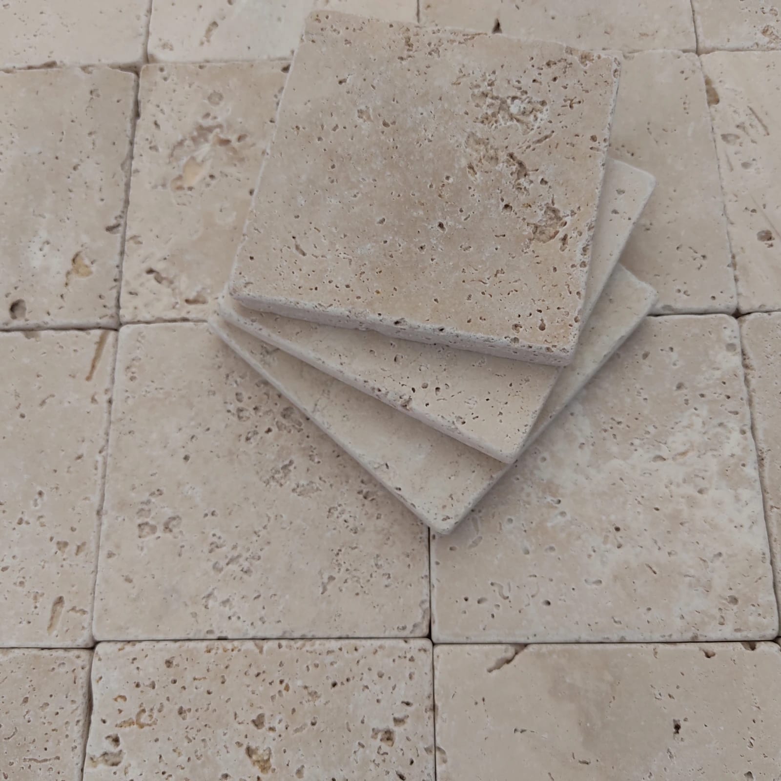 Photograph of overlapping thin pale travertine tiles, showing their natural pores and edges