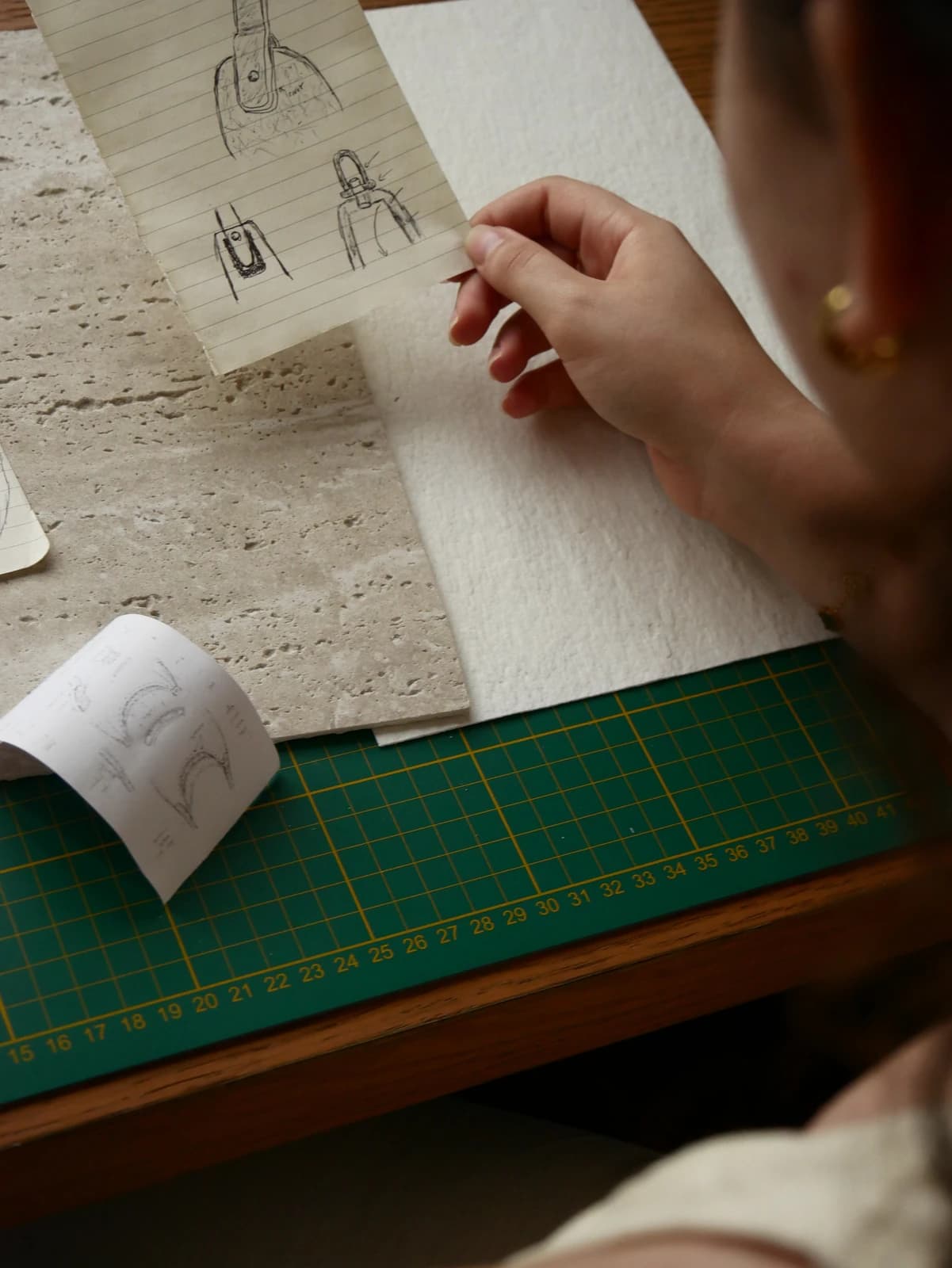 A hand holds sketches of the handle and attachments above stone and a cutting mat