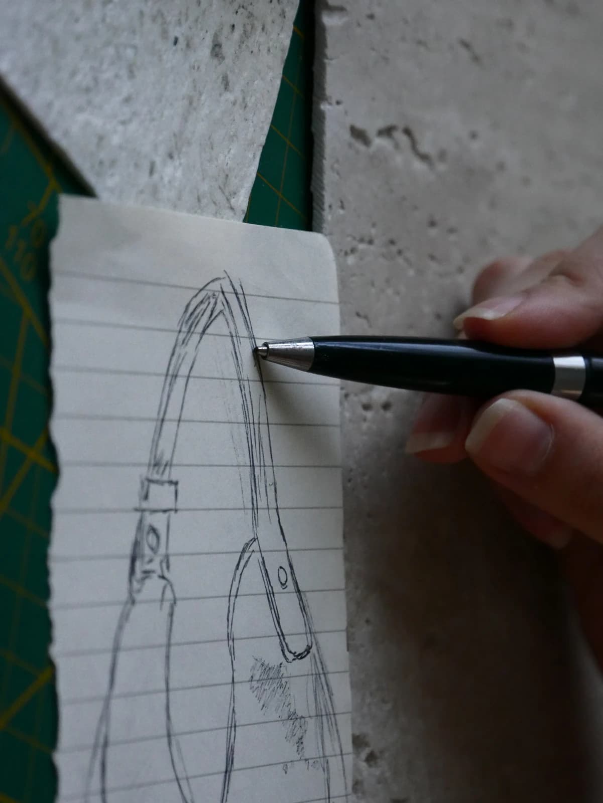 A hand traces the outline of PORTALE in pen on a sheet resting on travertine