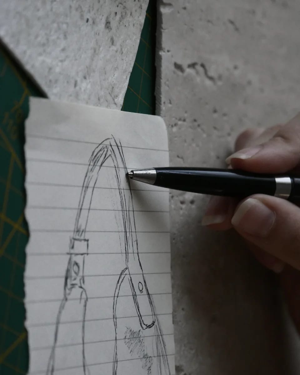 A hand tracing PORTALE’s handle in pen, on a stone slab